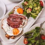 Top view of a brunch meal featuring fried eggs, bacon, fresh salad, and coffee.