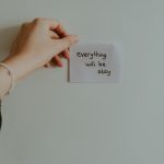 A hand holding a motivational note with uplifting text in an indoor setting.
